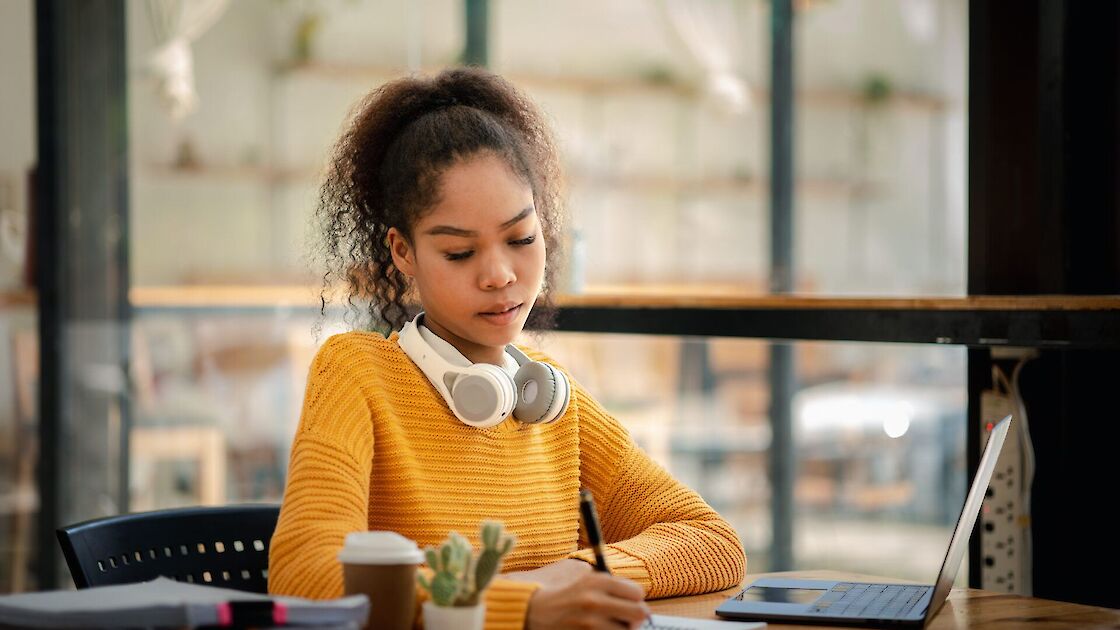 American teenage woman sitting in office with laptop, she is a student studying online with laptop at home, university student studying online, online web education concept.