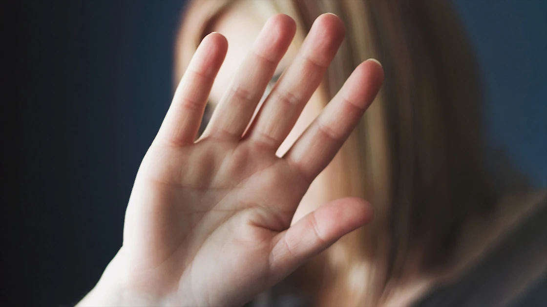 woman with hand raised, hiding her face